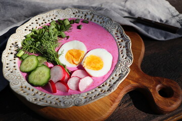 Cold beet soup with egg, cucumber, potatoes and greens on the wooden table. Speciality for hot days. Shallow depth of field, selective focus
