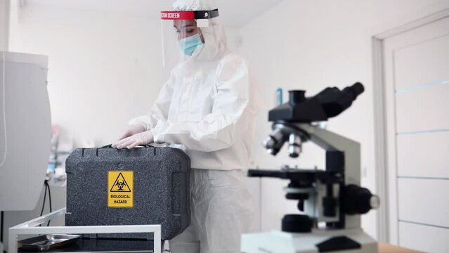 Clinic worker in safety uniform is in the lab with case. Biological hazard text on it