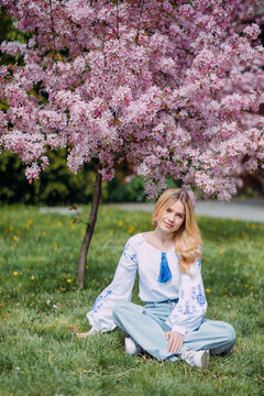 Young blonde woman rests on lawn near blooming sakura tree.
