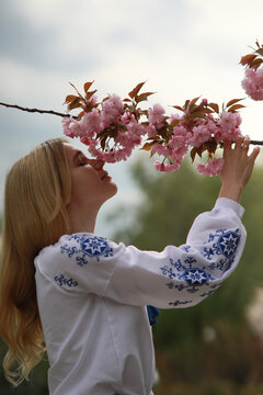 Young blonde woman sniffs blooming sakura branch and enjoys by it.