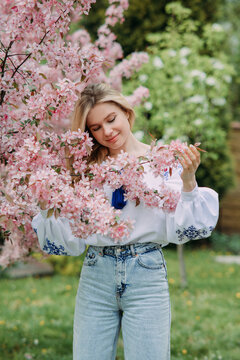Young blonde woman walks in garden and enjoys by blooming sakura trees.