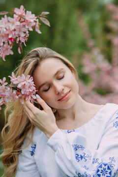 Portrait of young blonde woman in garden enjoying by blooming sakura trees.