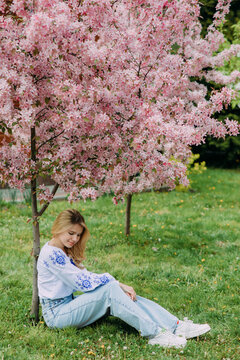 Young blonde woman rests on lawn near blooming sakura tree.