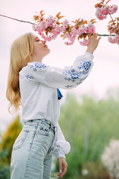 Young blonde woman sniffs blooming sakura branch and enjoys by it.