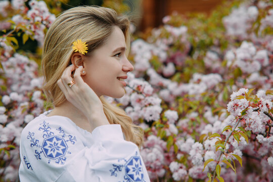 Portrait of young blonde woman in blooming sakura garden in Ukrainian embroidered shirt.
