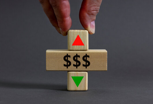 Dollar rates symbol. Businessman holds a wooden cube with arrow symbolizing that dollar rates are going down or up. Beautiful grey table grey background. Business and dollar rates concept. Copy space.