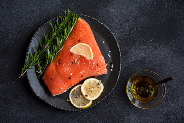 Uncooked raw salmon fish with herbs on dark background