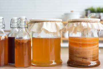 Homemade fermented raw kombucha tea, variety of flavors in bottles and glass jars mix with a fruit juice and scoby on wooden table. Healthy natural probiotic drink.