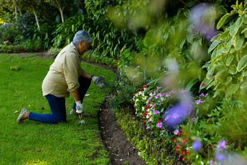 Side view of biracial senior woman with short hair gardening with fork tool while kneeling in yard