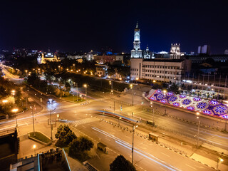 Fototapeta premium Aerial view on night city center streets with streetcar and cars driving in long exposure. Dormition Cathedral with illumination. Downtown streets in Kharkiv, Ukraine