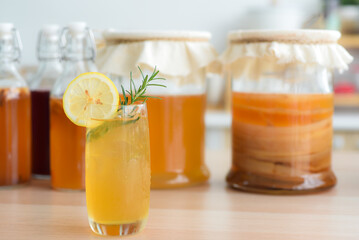 Kombu tea in a glass with ice, lemon slices and rosemary leaves, Homemade fermented raw kombucha tea in bottles and glass jars mix with fruit juice and scoby on table.Healthy natural probiotic drink.