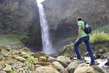 A man with a backpack is standing in front of a waterfall in Banos de Agua Santa, Cascada Manto de...