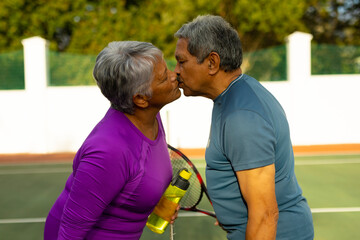 Side view of loving biracial senior couple with eyes closed kissing while standing at tennis court - Powered by Adobe