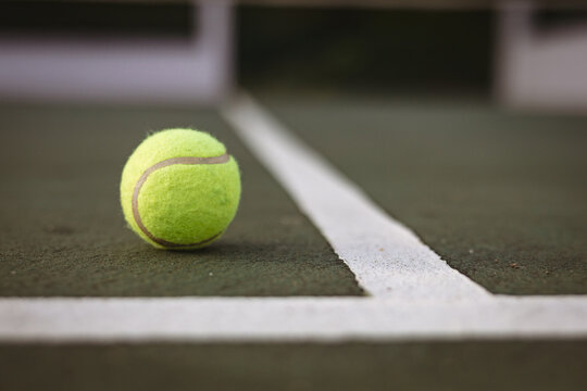 Close-up of yellow tennis ball by white lines on tennis court, copy space
