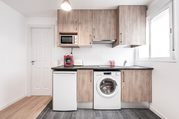 Kitchen with wood-colored cabinets, white appliances, dark countertops, and multi-colored hardwood floors