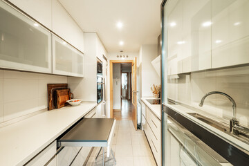 Kitchen with white furniture on both sides, removable folding table, column with appliances and glass door