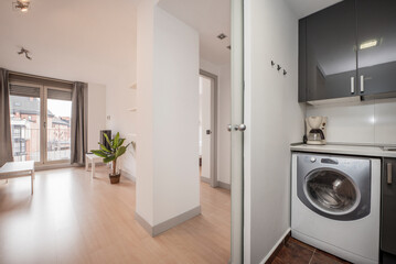 Kitchen with gloss gray cabinets, white countertop above washing machine, and living room with side tables