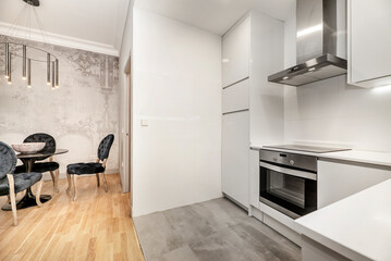 Apartment kitchen with white cabinets, white stone countertops, stainless steel range hood, gray ceramic tile floors, and living room with dining table