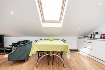 Dining table with green tablecloth under skylight in apartment with sloping ceilings