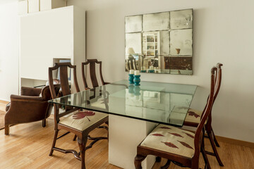 Glass dining table with one piece marble foot, wooden chairs and vintage mirror on the wall