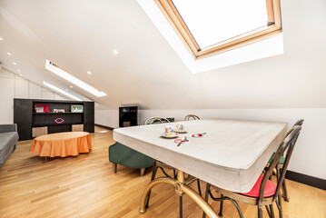 Wooden dining table with metal chairs under a sloping ceiling with skylights