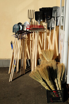 Gardening tools: shovels, rakes, brooms displayed against a wall on a sunny day. Storage or sale