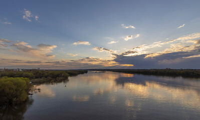 Evening landscape, sunset on the river. Wide river, horizon, clouds are reflected in the water. Sunlight through the clouds.