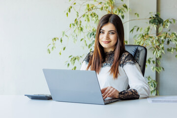 Portrait of a young business woman sitting at her workplace with a notebook, documents, calculator