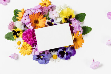 Festive card template. Spring and summer colorful flowers and blank paper sheet card mockup on white background. Flat lay, copy space for text, top view. Round frame wreath pattern.