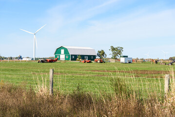 Modern green horse barn in a grassy field. Wind turbines are in background.