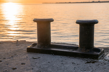 Close up of big steel bollards on a concrete pier in a harbour in warm sunset light in autumn....