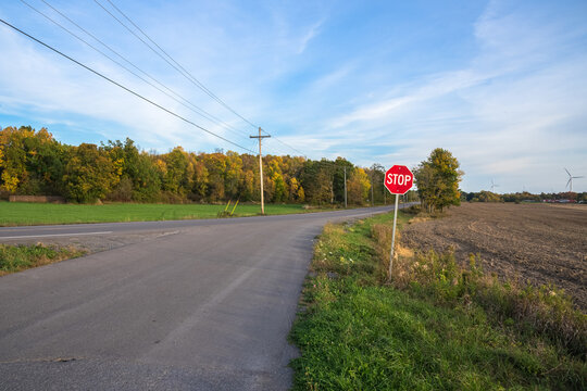 Stop sign at an intersection along a deserted country road at sunset. Wind turbines are visible in background.