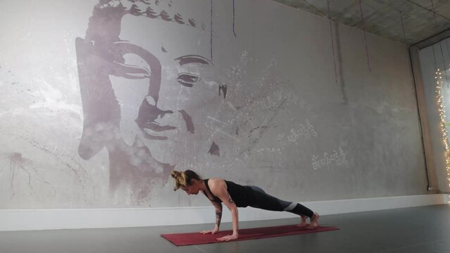 A woman with tattoos is engaged in aerobics against the background of a wall with the image of a Buddha