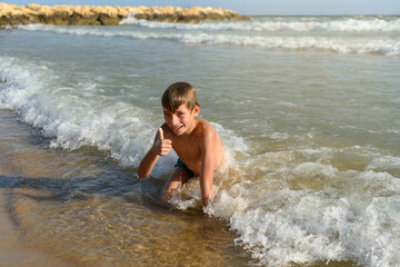Teenager smiles on the seashore, holding up his thumb