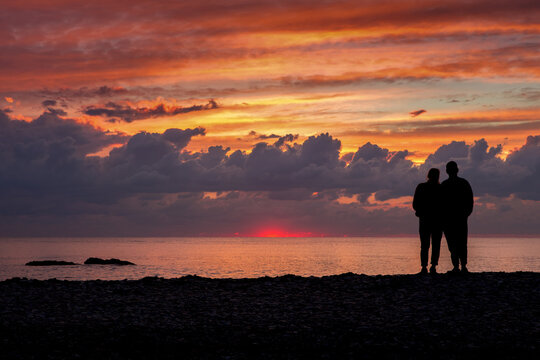 A couple in love stands on the shore and looks at the sunrise or sunset. Beautiful sky with clouds.