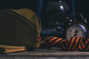 Russian soldiers cap,St. George ribbon, old book and an alarm clock with kerosene lamp. Victory Day is May 9th.