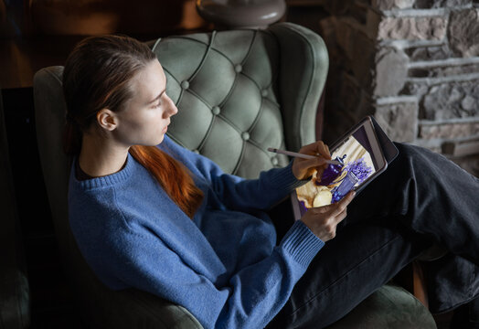 A girl sits in the lobby of a hotel or restaurant and draw the still life picture with teapot, lemon and flowers on electronic tablet. The concept of inspiration, creativity, self-development, hobby