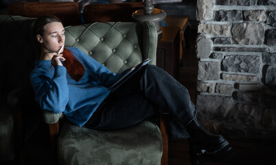 A girl sits in the lobby of a hotel or restaurant and draws or works on electronic tablet. The concept of inspiration, creativity, self-development, hobby, modern art. Modern technologies. Remote work