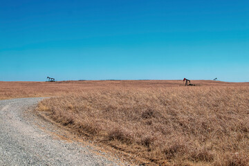 Three distant oil or gas well pumps on prairie grassland with curving gravel road running through it