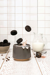 Splash spray of latte coffee cacao with milk and cookies falling in gray cup on white kitchen tile background, levitation floating food motion action