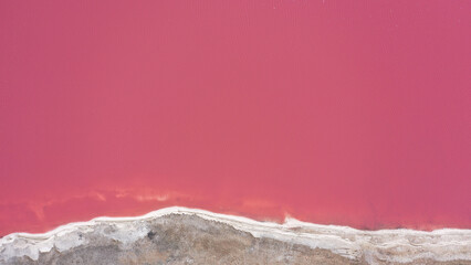 Flying over a pink salt lake. Salt production facilities saline evaporation pond fields in the salty lake. Dunaliella salina impart a red, pink water in mineral lake with dry cristallized salty coast.