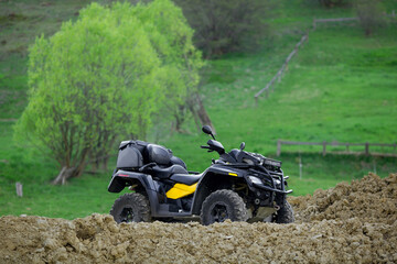 A four-wheeled ATV quad bike standing idle on the green grass, with trees and a mountain on the background.