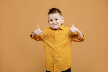 Portrait of funny clever school boy with headphones in yellow shirt. Yellow studio background. Education. Looking, smiling and shows a thumb up at camera. High quality photo