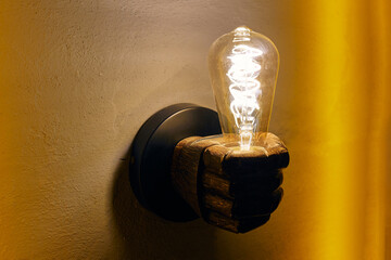 Hand shaped chandelier with glowing lightbulb on yellow wall