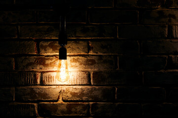 Bright glowing light bulb hangs near old grunge brick wall
