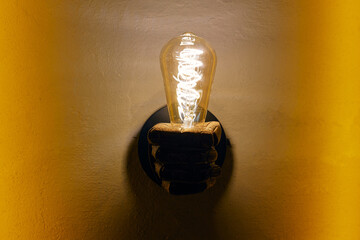 Fist shaped luster with glowing light bulb on yellow wall