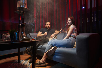 young man and woman sitting on the sofa and smoking a hookah in a hookah lounge in a relaxed atmosphere