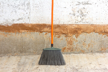 A large street cleaning broom stands against a concrete wall on the asphalt.