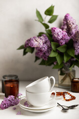Tea set against the background of a spring bouquet of lilacs on a textured gray background. Composition with books and candles. Side view. Place to copy.