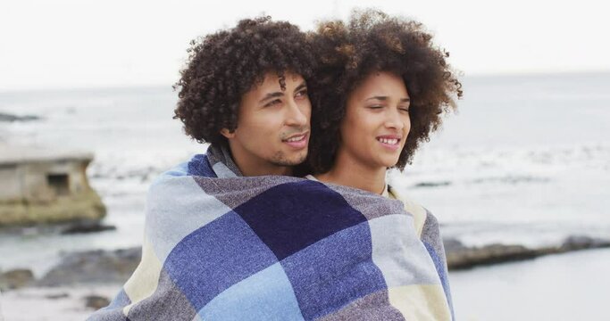African american couple wrapped in blanket on the promenade near the beach